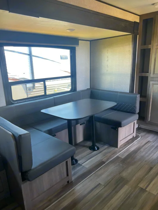 RV rental interior: a comfy U-shaped dinette with gray seating, table, and large window overlooking another RV.. Starcraft Autumn Ridge 2023