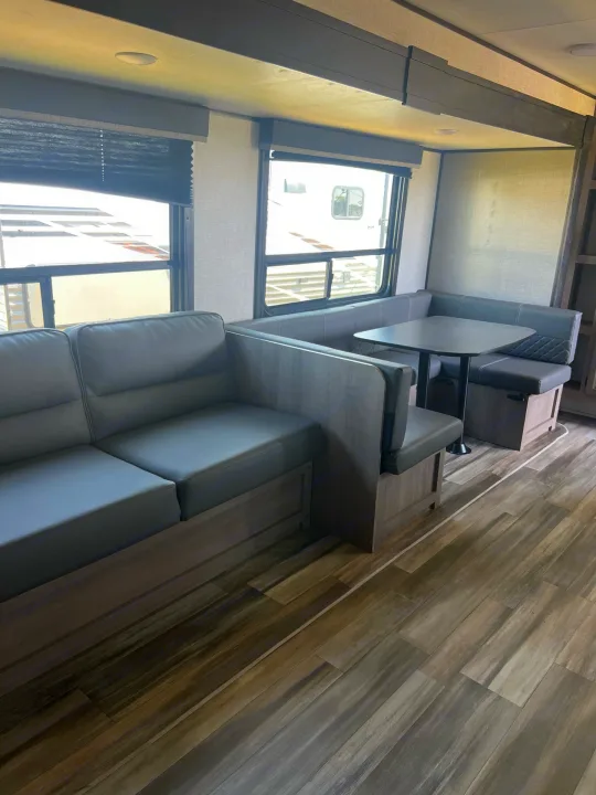 Spacious RV rental interior features a modern gray dinette, L-shaped seating, large windows, and stylish wood-look flooring.. Starcraft Autumn Ridge 2023