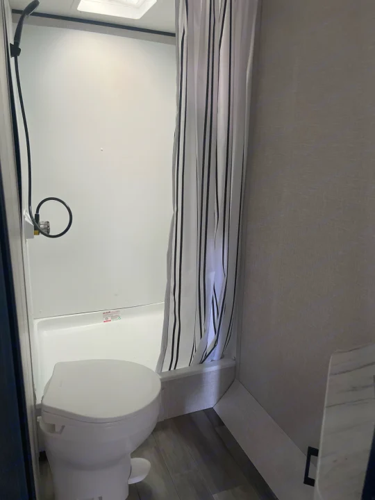 Compact RV rental bathroom: white toilet, shower stall with a striped curtain, and ceiling skylight.. Starcraft Autumn Ridge 2023