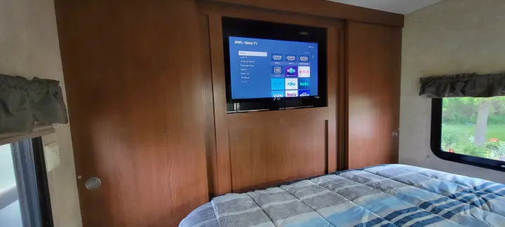 RV rental bedroom showing a built-in Roku TV with streaming apps over a comfortable bed.. Forest River Wildwood 2014