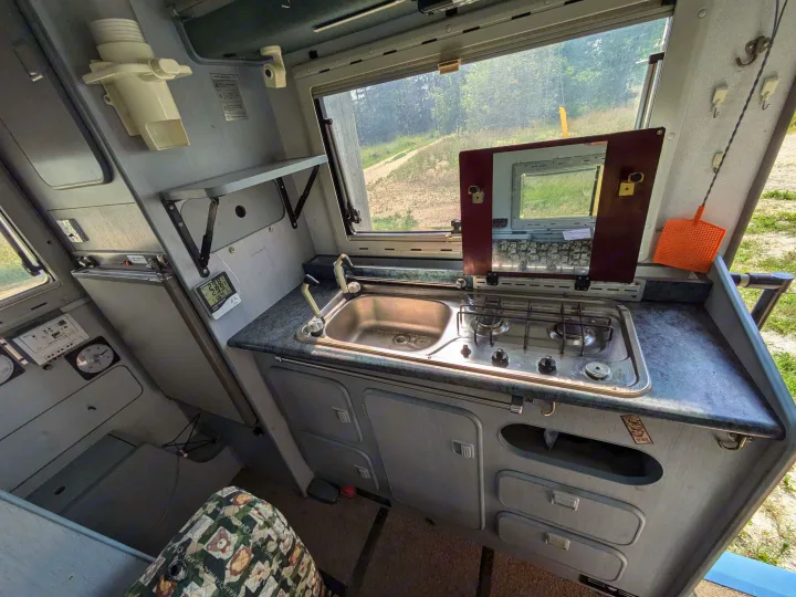 RV rental: Compact camper van kitchen with sink, two-burner stove, storage, and a scenic window view.. Mitsubishi Delica JB470 1996