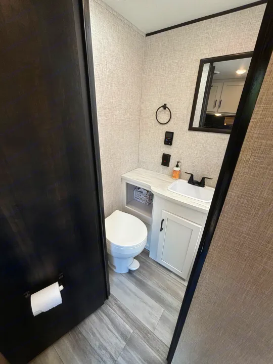 This modern RV rental features a compact bathroom with a toilet, sink vanity, and mirror, offering comfort on the go.. Jayco Jay Flight SLX 2024