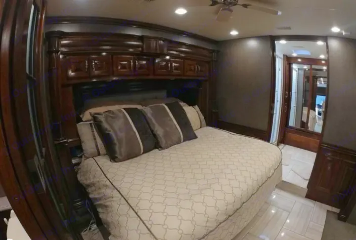 Luxurious RV rental bedroom features a spacious bed with patterned duvet, dark wood cabinetry, and a mirrored door.. American Coach Revolution 2017