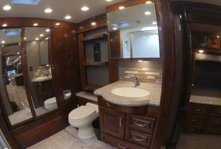 Inside a luxury RV rental: a spacious bathroom with a vanity, sink, toilet, and mirror reflecting a shower.. American Coach Revolution 2017