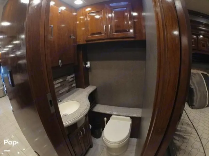 Discover this **RV rental**'s luxurious bathroom, featuring polished wood cabinetry, a vanity sink, and a compact toilet.. American Coach Revolution 2017