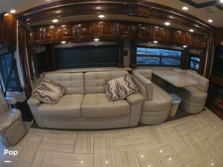Luxury RV rental interior featuring a beige sofa, dining booth, rich wood cabinetry, and tiled flooring.. American Coach Revolution 2017