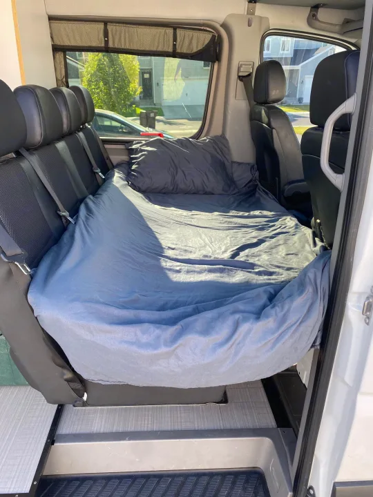 Inside an rv rental van: a comfortable bed setup, transforming passenger seats into a sleeping area for travel.. Mercedes-Benz Sprinter 2014