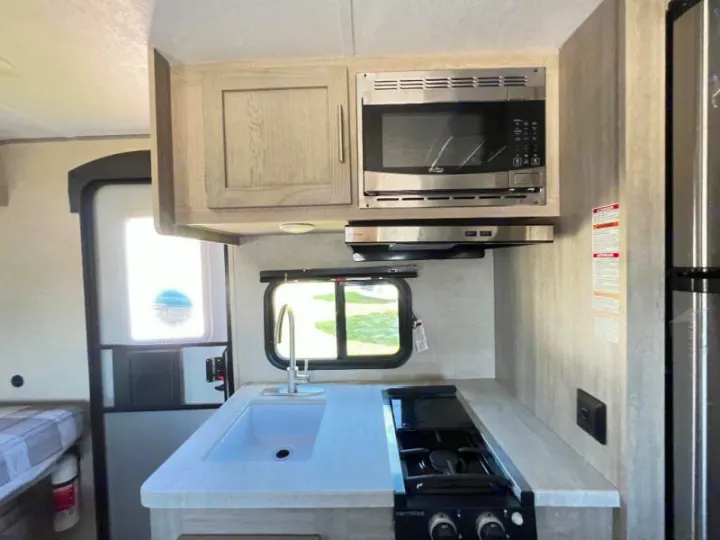 RV rental kitchen: modern compact design with microwave, stovetop, and sink for convenient travel meals.. Coachmen Catalina 2022