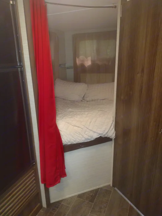 This rv rental showcases a compact, cozy bedroom with white bedding, pillows, and a vibrant red curtain for privacy.. Keystone RV Bullet Ultra Lite 2018