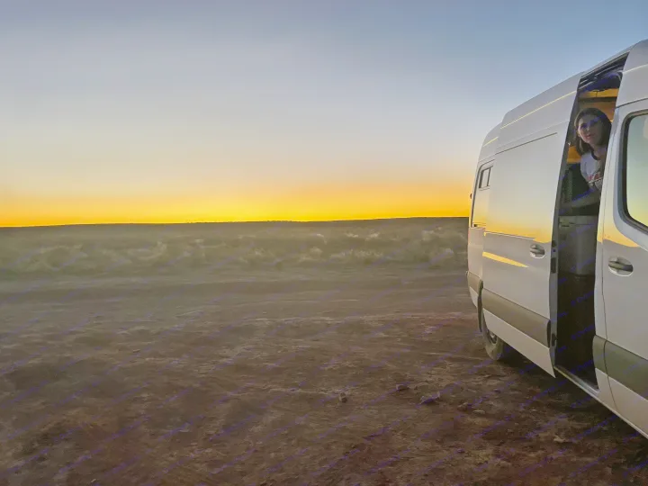 Sunset van life: An RV rental parked in desert at dusk, with a person peering out from the open side door.. Mercedes-Benz Sprinter-Loaded 2022