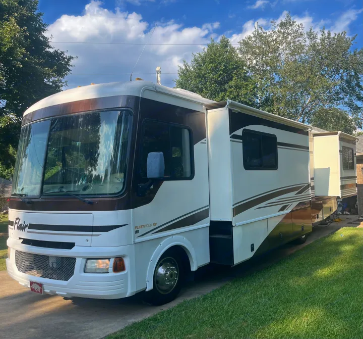A well-maintained brown & white RV rental motorhome with extended slide-outs, parked on a sunny driveway.. Fleetwood Flair 31A 2005