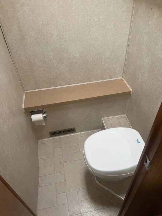 Compact RV rental bathroom with a white toilet, recessed paper holder, light patterned walls, and tiled floor.. Fleetwood Flair 31A 2005