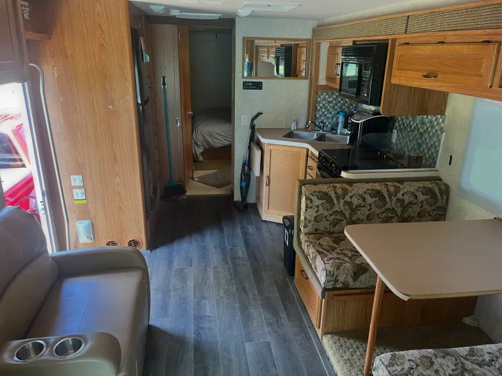 Interior of an rv rental, featuring a living area with a recliner, full kitchen, dinette, and a bedroom in the rear.. Fleetwood Flair 31A 2005