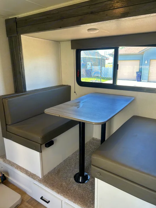 RV rental interior: A bright dinette with dark grey benches, a light wood table, and a large window.. Keystone RV Hideout 2022