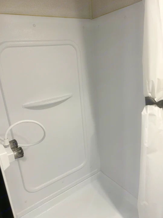 This clean, compact shower in an RV rental features a handheld sprayer, built-in shelf, and a neatly tied-back curtain.. Keystone RV Hideout 2022
