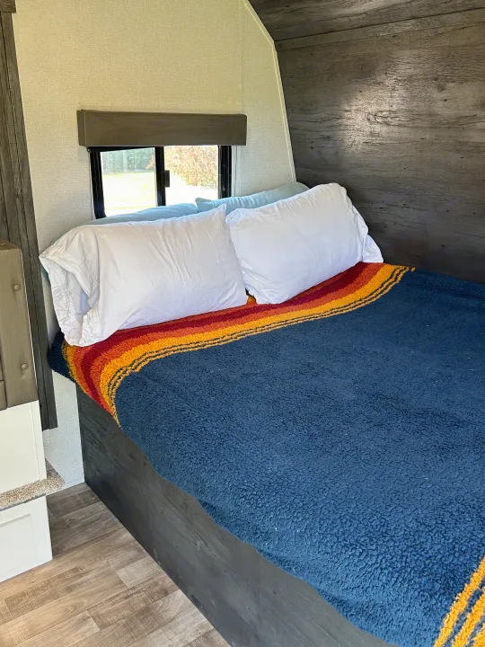 Cozy RV rental bedroom with striped blanket, white pillows, wood accents, and window view.. Keystone RV Hideout 2022