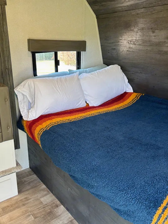 Cozy RV rental bedroom: bed with white pillows, blue, red, orange striped blanket, and window view.. Keystone RV Hideout 2022