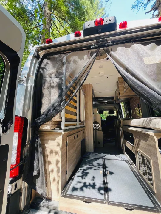 Spacious RV rental interior: A camper van ready for adventure with its open back doors, mesh screen, and custom wood cabinetry.. Winnebago Eurovan Camper Eurovan Camper 2023