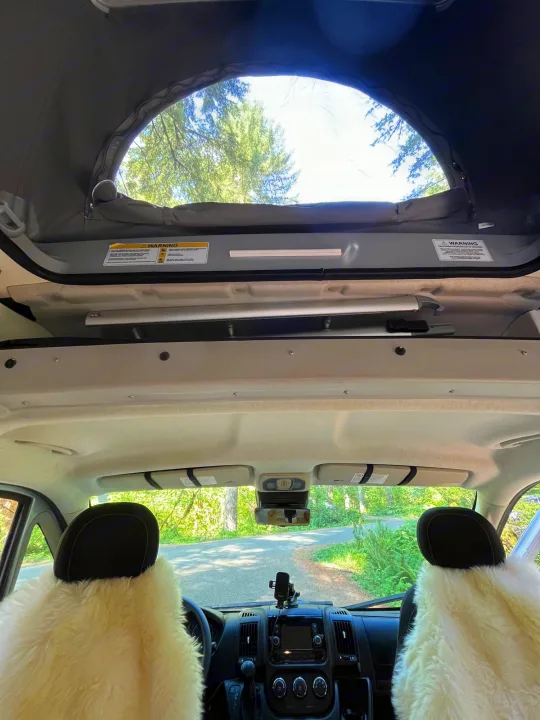View from inside an RV rental looking forward, showing the open pop-top roof, fluffy front seats, and a road ahead.. Winnebago Eurovan Camper Eurovan Camper 2023