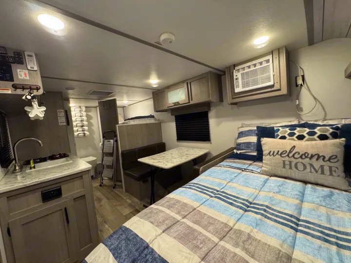 Discover this cozy RV rental interior, featuring a kitchen, dining booth, and comfortable bed with a 'Welcome HOME' pillow.. Coleman Lantern LT 17B 2024