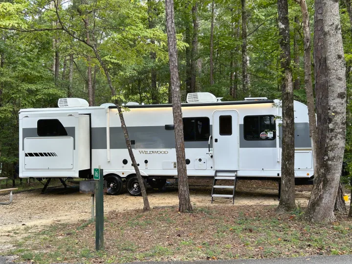 Wildwood travel trailer RV rental at a serene wooded campsite, featuring an extended slide and entry steps.. Forest River RV Wildwood 31KQBTSX 2025