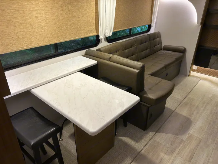 Comfortable RV rental living space with L-shaped sofa, expandable dining table, and modern interior design for travel.. Forest River RV Wildwood 31KQBTSX 2025
