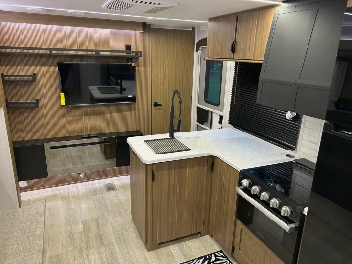 Modern RV rental interior showcasing a well-equipped kitchen, TV, and stylish wood paneling.. Forest River RV Wildwood 31KQBTSX 2025