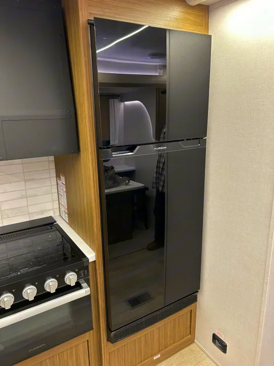 Modern RV kitchen interior featuring a black Furrion refrigerator, stove, and oven. Ideal for your next rv rental adventure.. Forest River RV Wildwood 31KQBTSX 2025