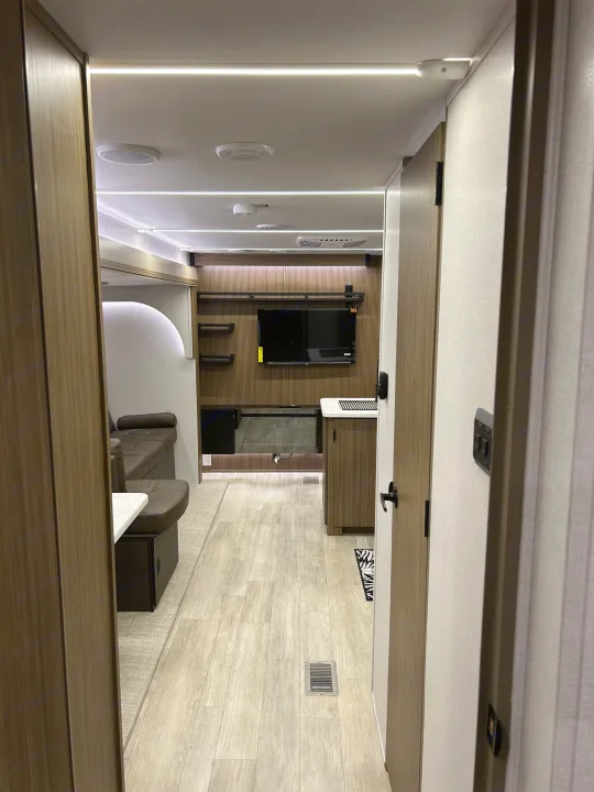 RV rental interior showing a modern living area from a doorway, featuring strip lighting, a wall-mounted TV, and a dinette.. Forest River RV Wildwood 31KQBTSX 2025