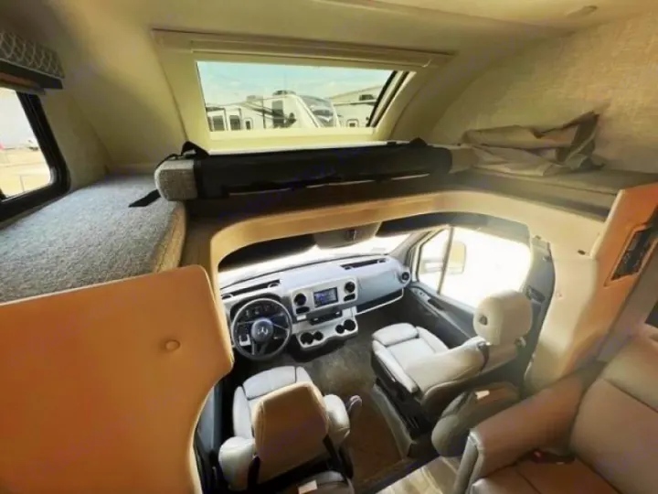 Inside a modern RV rental: view of the driver's cockpit, overhead bunk, and a side sleeping area.. Thor Quantum 2022