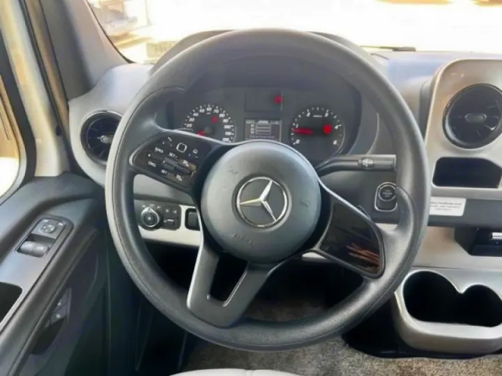 Interior view of a modern RV rental. Features a Mercedes steering wheel, dashboard with gauges, door controls, and cup holders.. Thor Quantum 2022