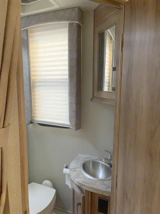 Inside an RV rental: a compact bathroom featuring a toilet, sink, mirror, and window. Practical amenities for travel.. Entegra Coach Odyssey 2019