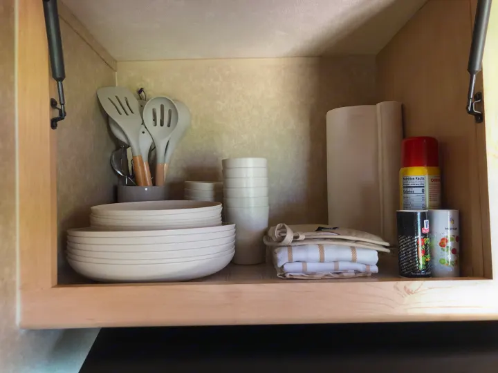 RV rental kitchen cabinet featuring compact storage: plates, bowls, utensils, cooking essentials, and towels.. Forest River Rockwood Mini Lite 2012