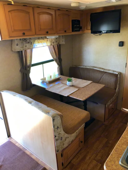 Functional RV rental interior featuring a dinette with bench seating, overhead cabinets, and a TV.. Forest River Rockwood Mini Lite 2012