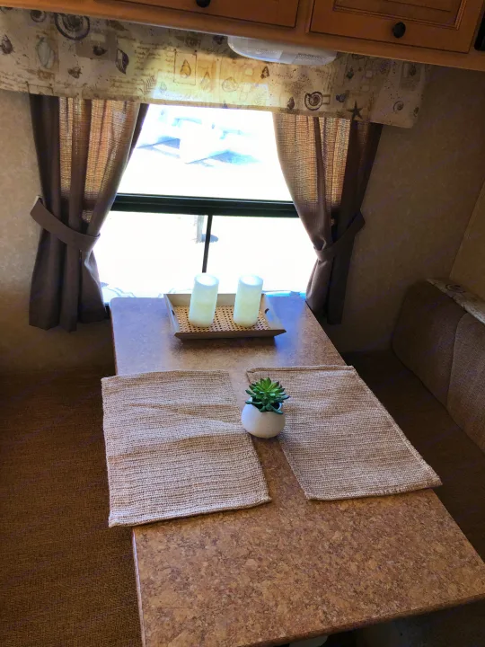 RV rental dining area with brown booth seating, curtains, and a table featuring candles and a succulent plant.. Forest River Rockwood Mini Lite 2012