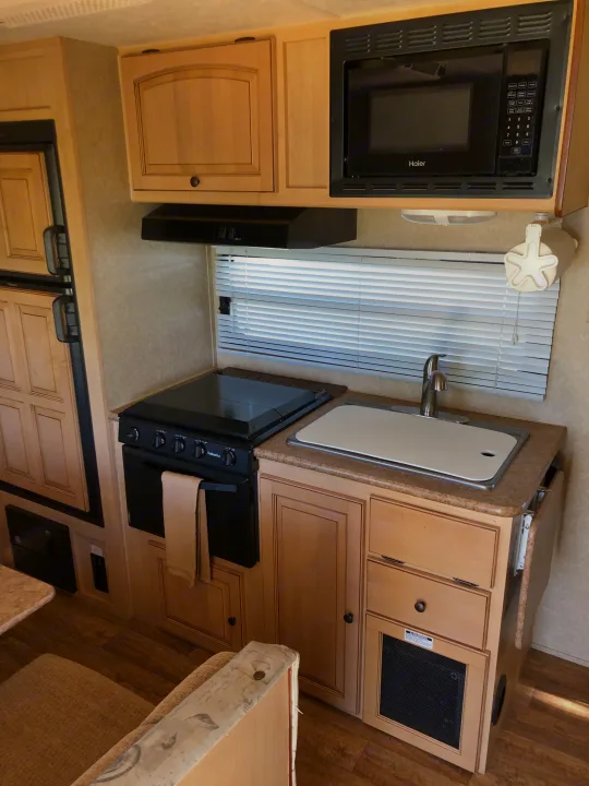 Compact RV rental kitchen, featuring Haier microwave, Suburban stove, sink, and light wood cabinets. Equipped for travel.. Forest River Rockwood Mini Lite 2012