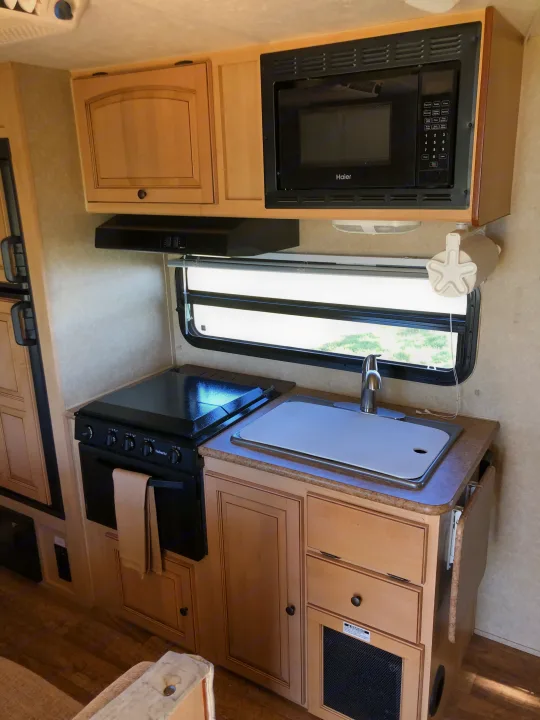 Well-equipped RV kitchen with microwave, oven, sink, and ample storage cabinets, ready for your RV rental adventure.. Forest River Rockwood Mini Lite 2012