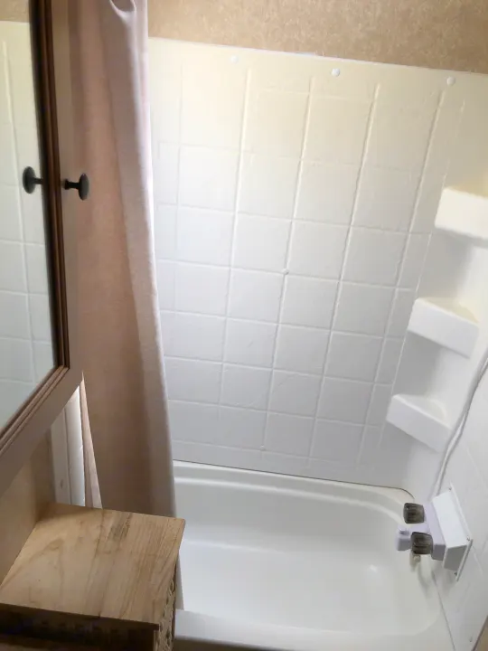 RV rental bathroom featuring a compact white tub/shower, built-in shelves, and a beige shower curtain.. Forest River Rockwood Mini Lite 2012