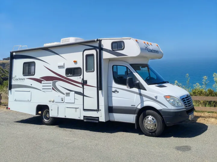 A white Coachmen Freelander rv rental parked on an asphalt road with a clear blue ocean view under sunny skies.. Forester Forester Motorhome 2019