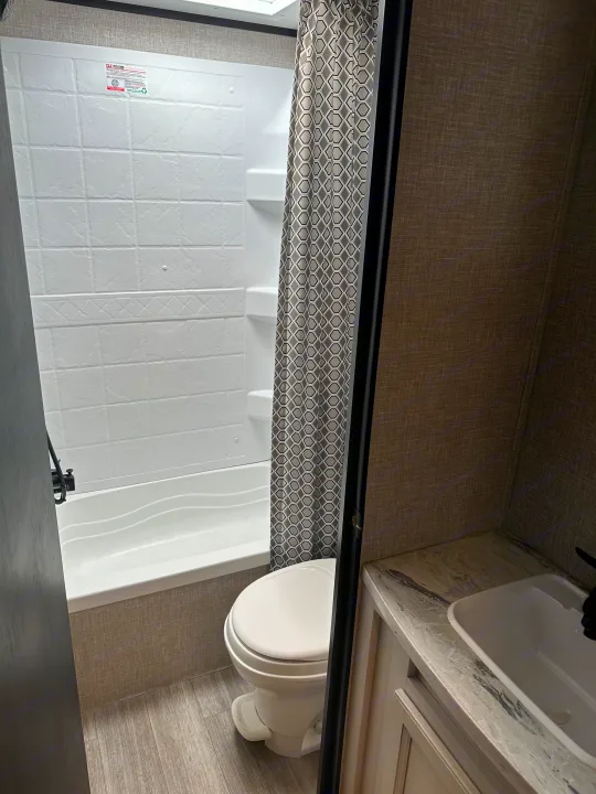 Compact RV rental bathroom featuring a tub/shower combo, toilet, and sink vanity with a patterned shower curtain.. Jayco Jay Flight 2022