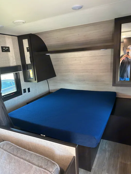 Cozy RV rental bedroom with blue bed, light wood paneling, and overhead storage for a comfortable stay.. Jayco Jay Flight 2022