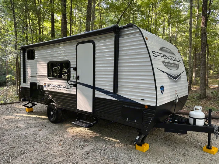 Springdale Keystone RV rental travel trailer parked on gravel in woods, set up for camping.. Keystone RV Springdale 2024