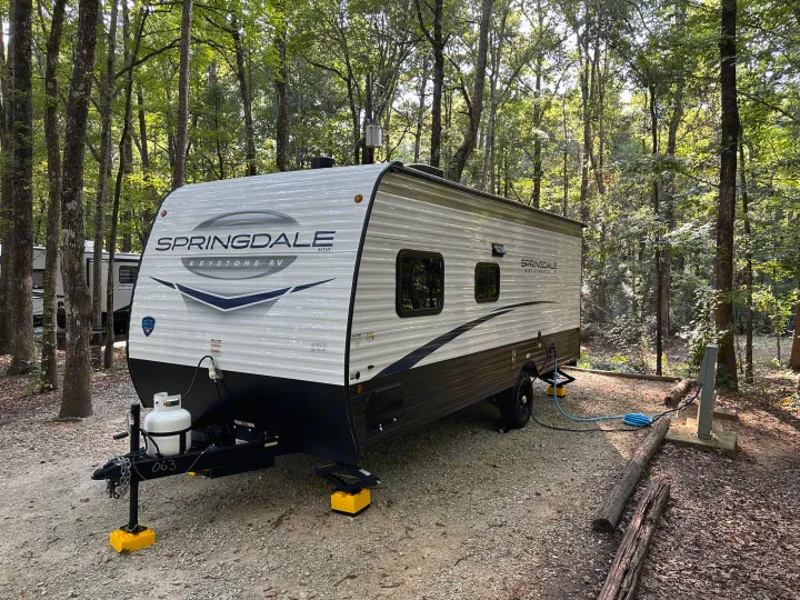 This RV rental, a Springdale travel trailer, is set up at a wooded campground, ready for a peaceful nature escape.. Keystone RV Springdale 2024
