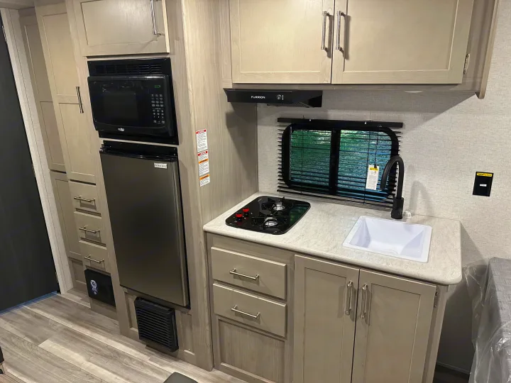 Compact RV rental kitchen features microwave, fridge, stovetop, and sink. Ideal for travel cooking.. Keystone RV Springdale 2024
