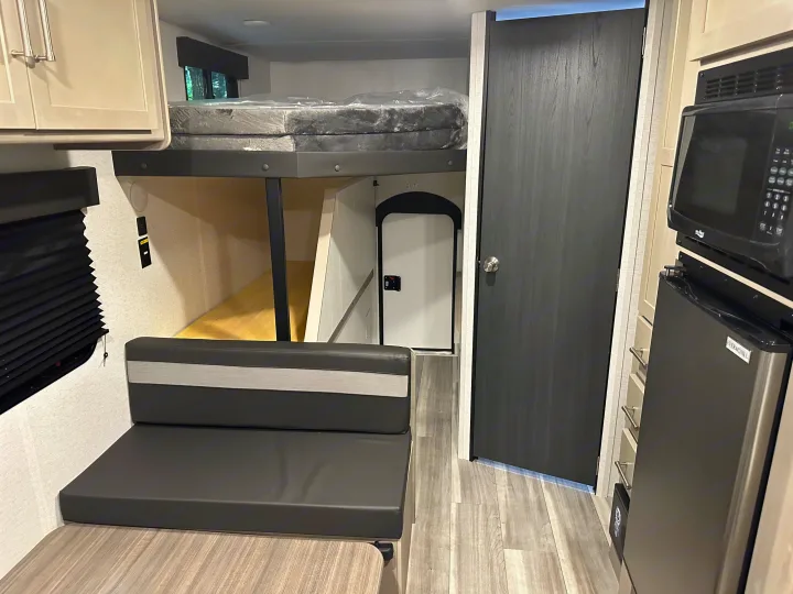 Explore this cozy RV rental interior with bunk bed, dinette, and compact kitchen featuring a microwave & fridge.. Keystone RV Springdale 2024