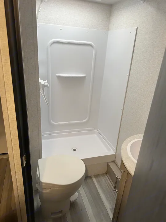 This RV rental's compact bathroom features a white shower stall, toilet, and small vanity with sink.. Keystone RV Springdale 2024