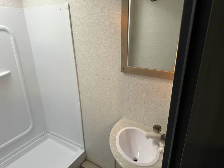 Inside an RV rental: a compact bathroom with a white shower, vanity sink, and mirror. Ideal for your travel adventures.. Keystone RV Springdale 2024