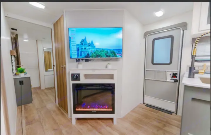 RV rental interior featuring a TV, electric fireplace, modern kitchen area, and main entry door. A comfortable living space.. Heartland RVs Eddie Bauer BHS 34 2024
