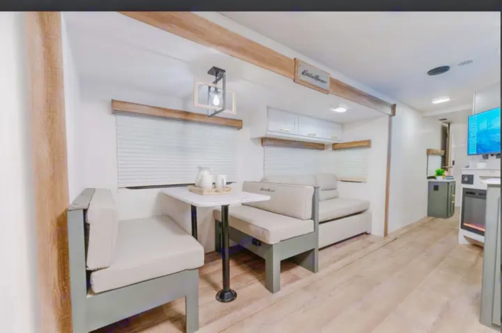 Modern RV rental interior with light wood accents. Features a dinette, comfortable sofa, and TV setup for cozy travels.. Heartland RVs Eddie Bauer BHS 34 2024