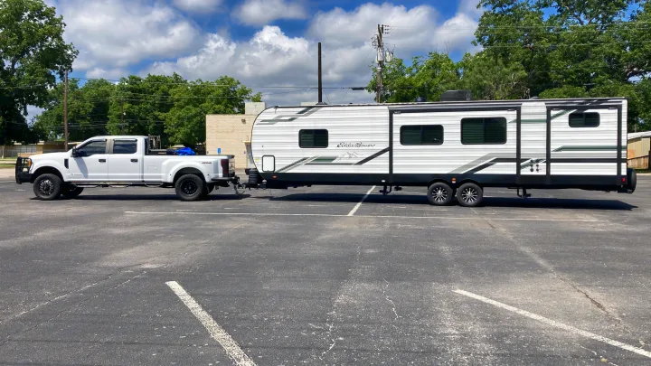 A white truck tows a large white Eddie Bauer travel trailer in a sunny parking lot. Ideal for your next RV rental adventure.. Heartland RVs Eddie Bauer BHS 34 2024